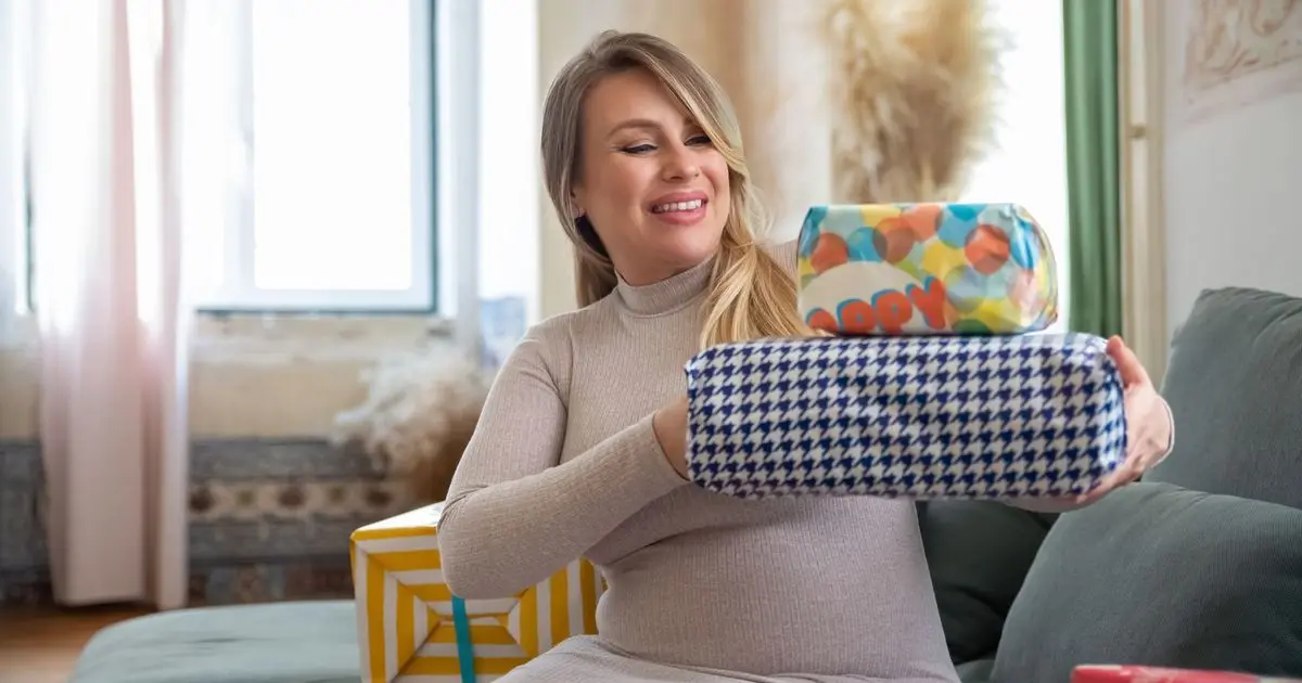 Gestante sorrindo com presentes embrulhados nas mãos